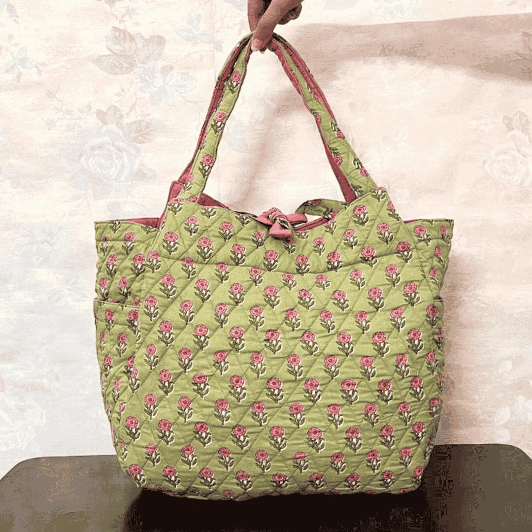 Handcrafted green quilted cotton tote bag with pink floral block print and tie-knot closure, held by hand